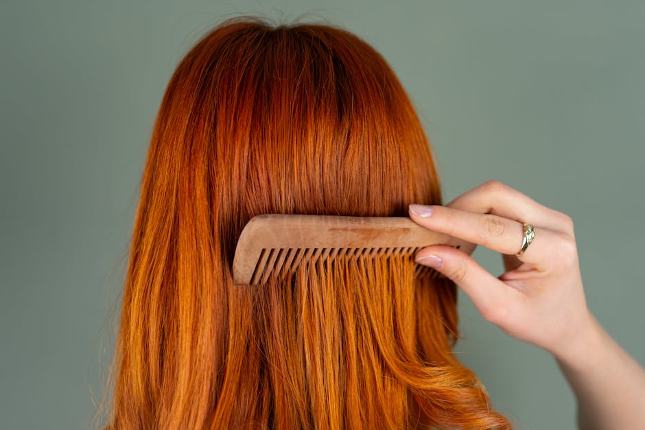 Close-up of a woman's red hair being combed with a wooden comb, capturing the smooth texture.