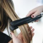 Close-up of a hairstylist using a flat iron on blonde hair in a salon setting.