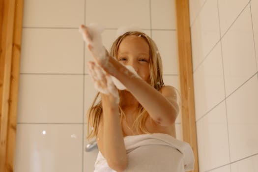 A happy young girl enjoys bath time, playing with foamy bubbles indoors.